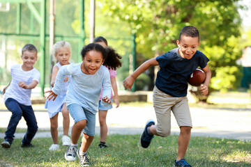 Cute little children playing with rugby ball in park