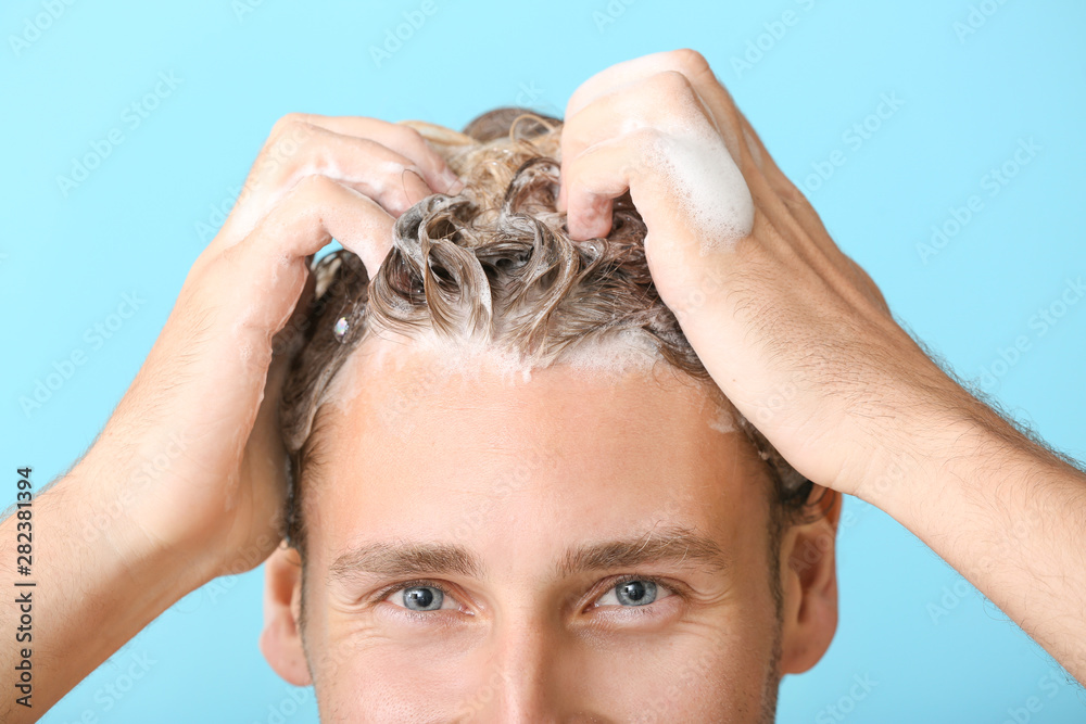 Fototapeta premium Handsome young man washing hair against color background, closeup