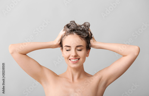 Beautiful young woman washing hair against grey background