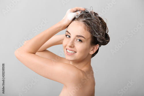 Beautiful young woman washing hair against grey background