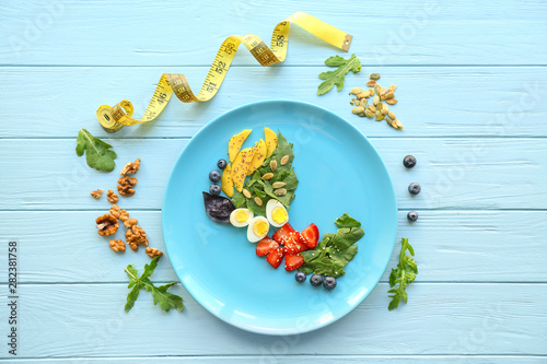 Plate with ingredients for fresh tasty salad and measuring tape on wooden background. Weight loss concept