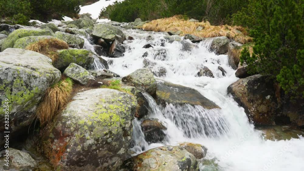 Small mountain creek, in winter, snow still visible over some rocks. Detail on water flowing over rocks during overcast spring day Small mountain creek, in winter, snow still visible over some rocks. Detail on water flowing over rocks during overcast spring day