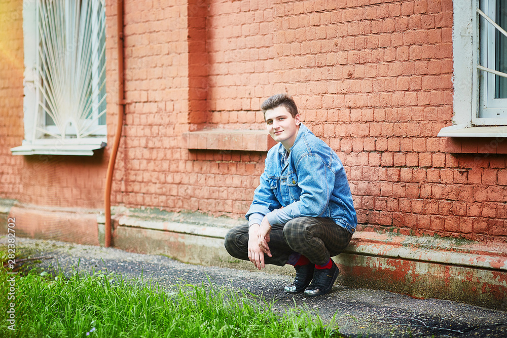 handsome caucasian guy squatting near an old brick wall of a building. handsome caucasian guy squatting near an old brick wall of a building.