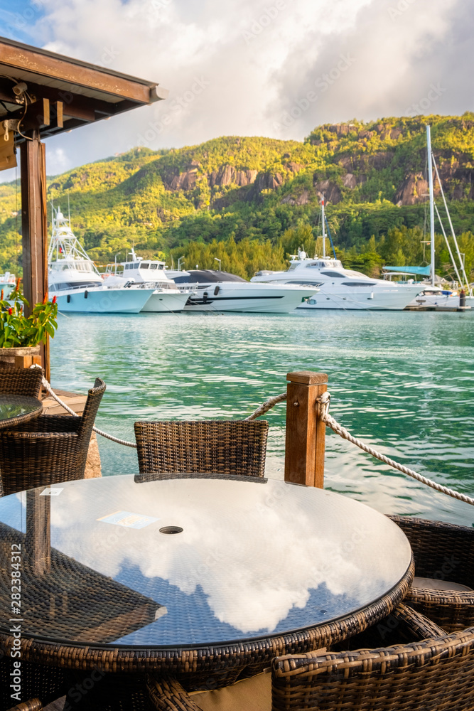 Round table by Luxury yachts and Boats marina in sunny summer day of Eden Island, Mahe, Seychelles vertical composition