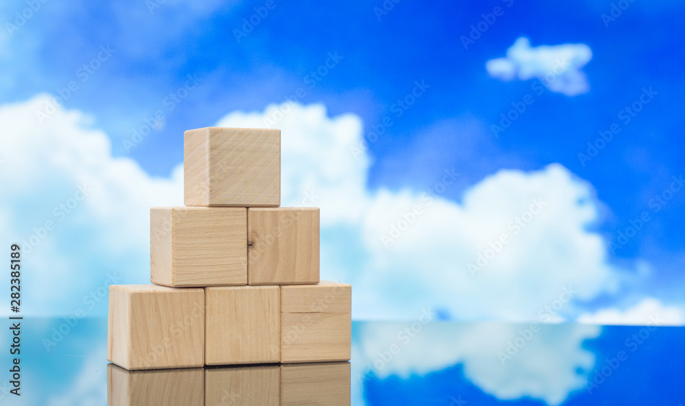 Pyramid of wooden cubes against the blue sky. Wooden cube Stacked in Pyramid shape without graphics for Business and design concept, Symbol of leadership, Teamwork and Growth. Pyramid of wooden cubes against the blue sky. Wooden cube Stacked in Pyramid shape without graphics for Business and design concept, Symbol of leadership, Teamwork and Growth.