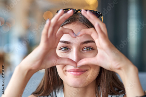 Beautiful woman looking through heart gesture made with hands photo