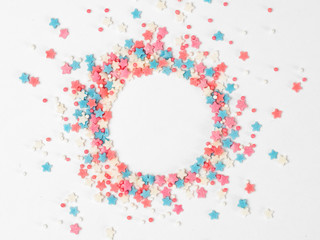 Festive border frame of colorful pastel sprinkles on white background with copy space in center. Sugar sprinkle dots and stars in round shape, decoration for cake and bakery. Top view or flat lay