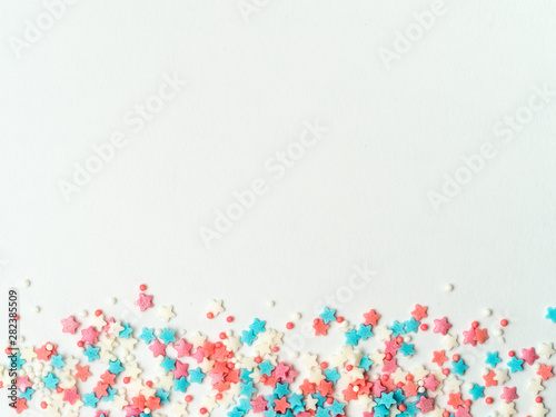 Festive border frame of colorful pastel sprinkles on white background, copy space top. Sugar sprinkle dots and stars, decoration for cake and bakery. Top view or flat lay