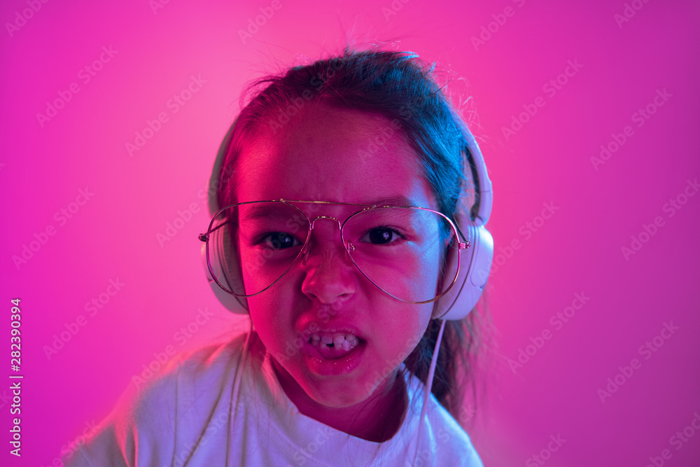 Beautiful female half-length portrait isolated on purple backgroud in neon light. Emotional girl in eyeglasses. Human emotions, facial expression concept. Dancing, listening to music, singing