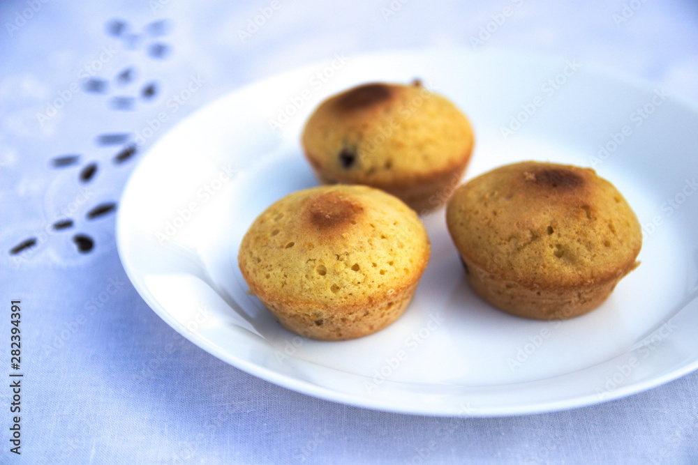 Muffins lie on a white plate on a blue tablecloth Muffins lie on a white plate on a blue tablecloth
