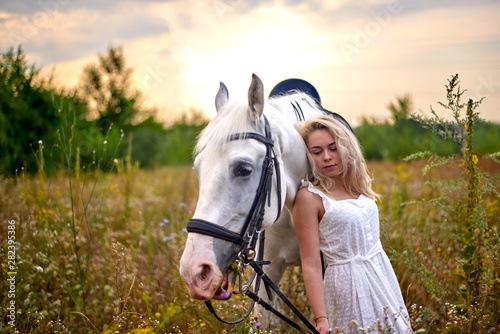 Girl in white dress holding a horse in the field