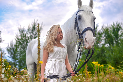 Girl in white dress holding a horse in the field