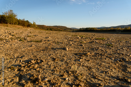 The bed of the dried-up river in the light of the setting sun  with clouds in the sky  with mountains in the background  shot during the season of golden autumn. Yellow-golden-brown.