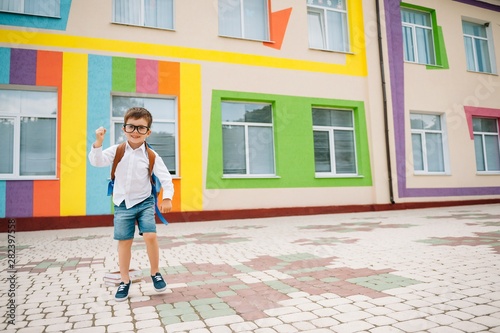 Back to school. Happy smiling boy in glasses is going to school for the first time. Child with backpack and book outdoors. Beginning of lessons. First day of fall. © Serhii