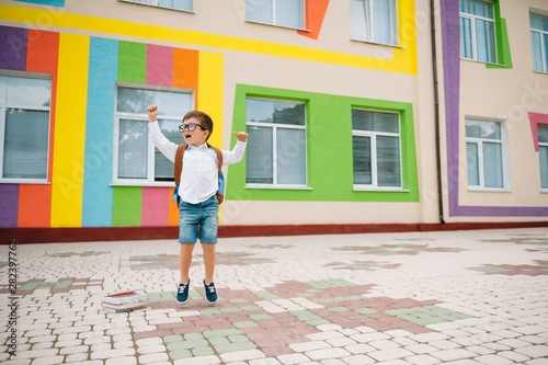 Back to school. Happy smiling boy in glasses is going to school for the first time. Child with backpack and book outdoors. Beginning of lessons. First day of fall.