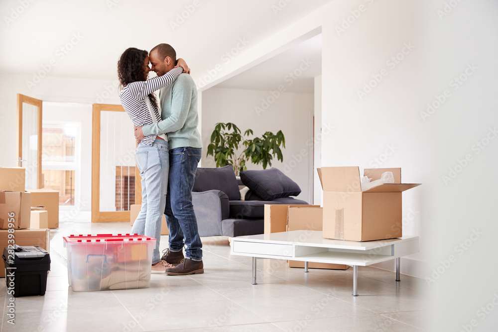 Loving Couple Hugging Surrounded By Boxes In New Home On Moving Day Loving Couple Hugging Surrounded By Boxes In New Home On Moving Day