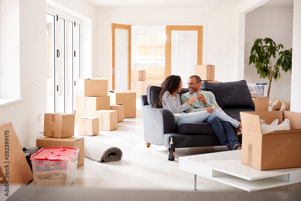 Couple Taking A Break And Sitting On Sofa Celebrating Moving Into New Home With Champagne Couple Taking A Break And Sitting On Sofa Celebrating Moving Into New Home With Champagne