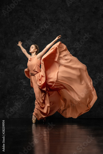 Ballerina. A young dancer dressed in a long peach dress picked up the edge of dress and raised up your hands in a butterfly pose. Performs a graceful, graceful dance movement. Beautiful classic ballet