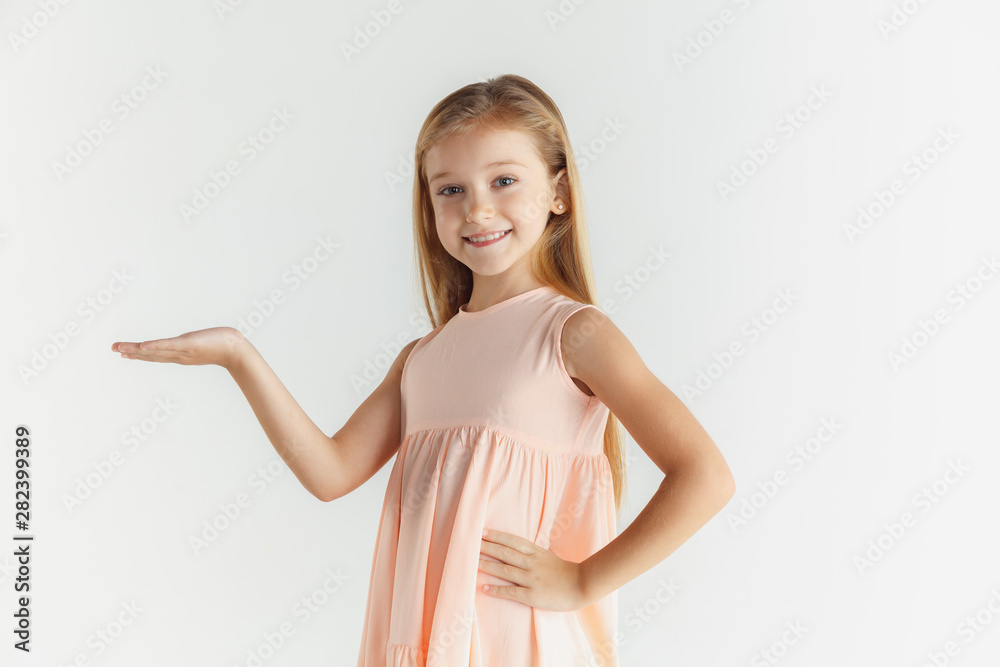 Stylish little smiling girl posing in dress isolated on white studio background. Caucasian blonde female model. Human emotions, facial expression, childhood. Showing on empty space bar. Stylish little smiling girl posing in dress isolated on white studio background. Caucasian blonde female model. Human emotions, facial expression, childhood. Showing on empty space bar.