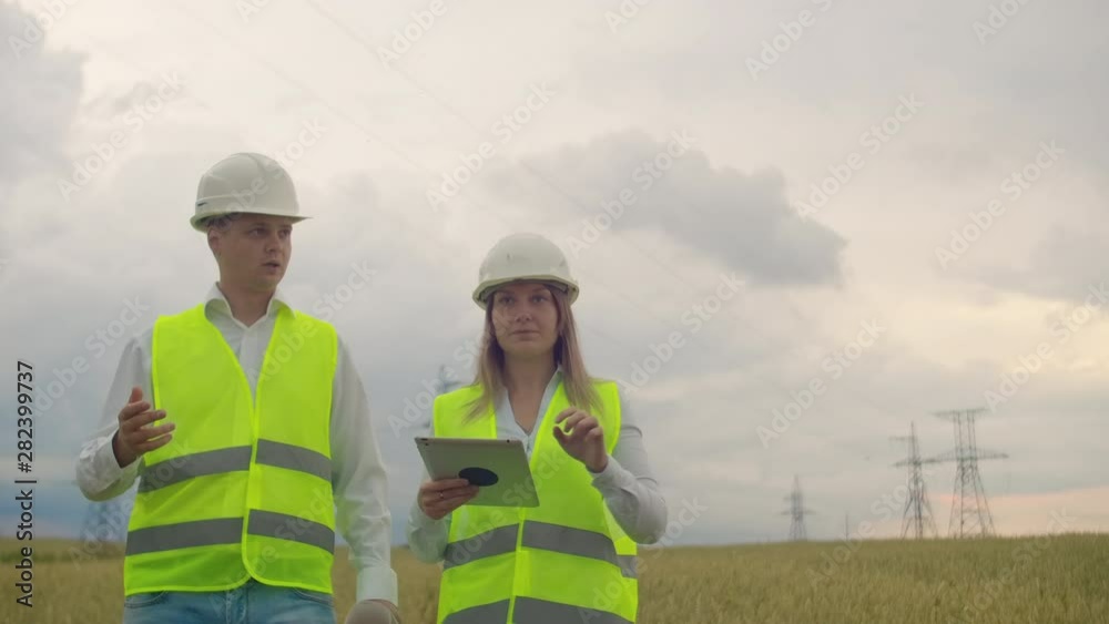 Power lines, man and woman engineers with a tablet in their hands check the progress of the installation of new towers and analyze the network. Power lines, man and woman engineers with a tablet in their hands check the progress of the installation of new towers and analyze the network.