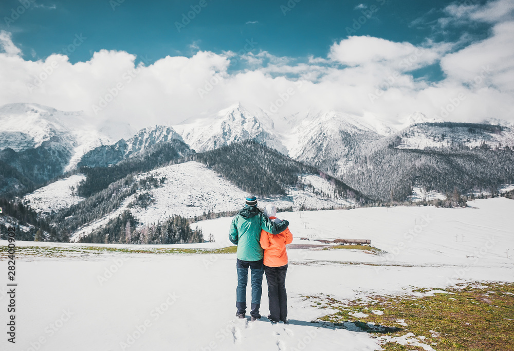 Loving couple standing and looking on beautiful snowy mountains peaks. Panoramic view. Back view.