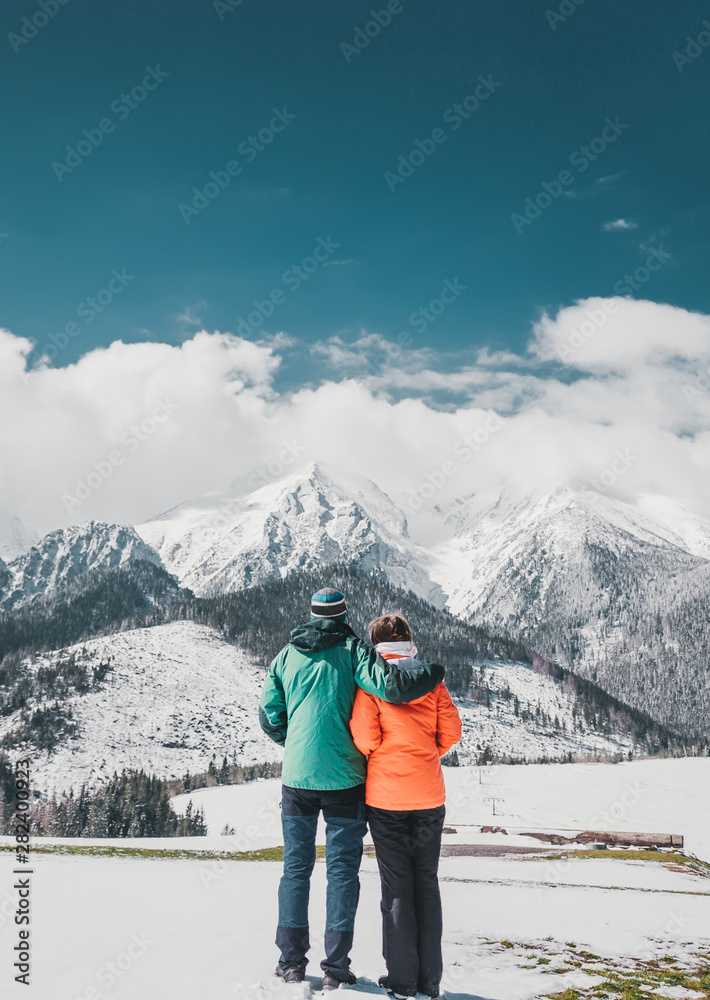 Loving couple standing and looking on beautiful snowy mountains peaks. Vertical panoramic view. Back view.
