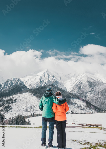 Obraz na płótnie Loving couple standing and looking on beautiful snowy mountains peaks. Vertical panoramic view. Back view. w salonie