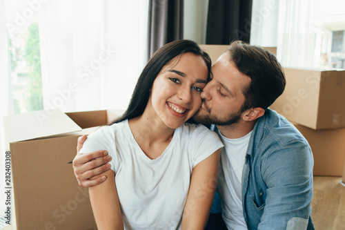 Mixed race couple happy moving at new home. Man and woman hugging and sitting on floor near cardboard boxes © Peakstock