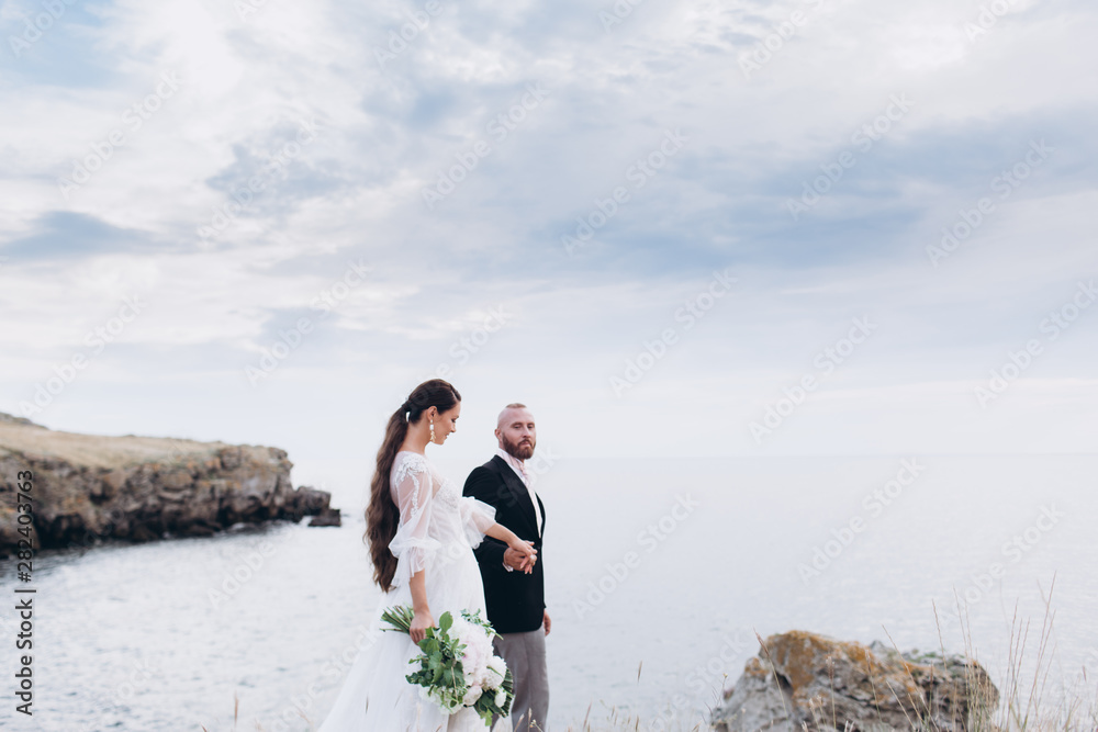 The bride and groom hugging and kissing on the background of the sea and rocks. 