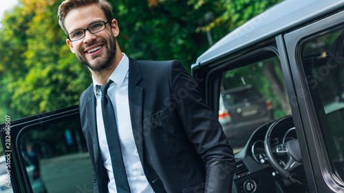 Handsome smiling young businessman coming out of his car while standing outdoors © InsideCreativeHouse