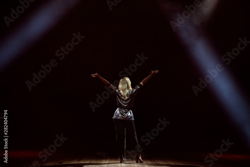 A young woman singer on stage during a concert view from the back.