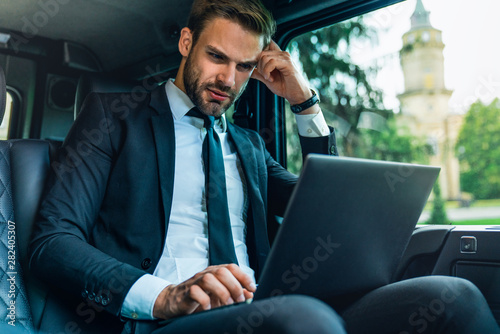 Thoughtful young man in full suit working using laptop and holding his head by hand while sitting in the car © InsideCreativeHouse
