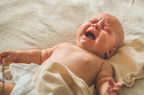 Leinwand Poster Crying hungry newborn baby lying on the bed