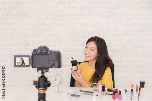Beauty blogger beautiful young woman wearing a yellow shirt Is sitting in front of a DSLR camera recording video clip review makeup and cosmetics recommendations.