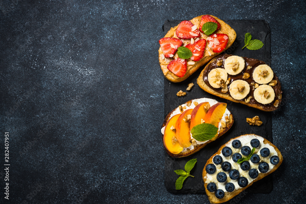 Sweet toast assortment with fresh fruit and berries on black.