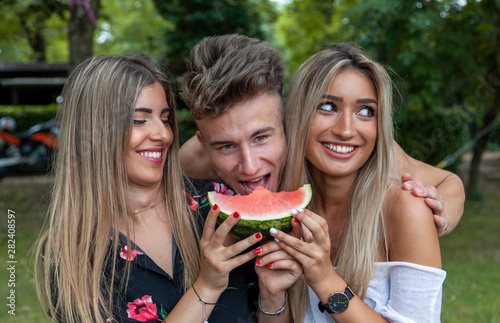 three young and beautiful people they eating a slice of fresh and juicy watermelon
