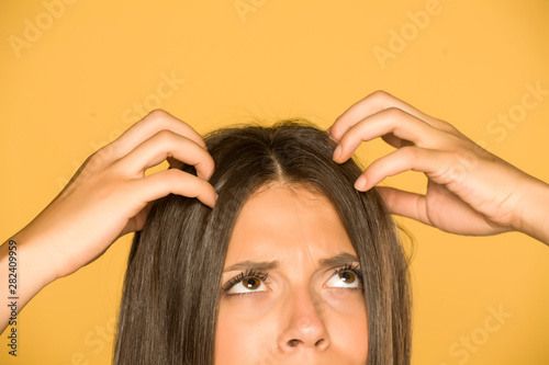 Beautiful young woman with itchy scalp on yellow background photo