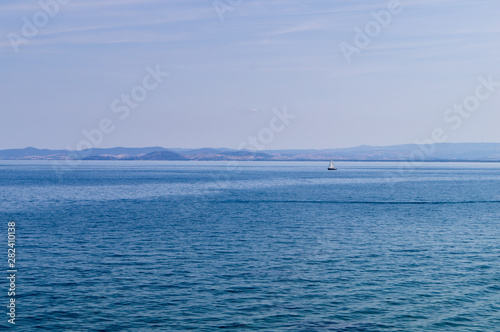 Panorama of the Tuscan sea with a sailboat.