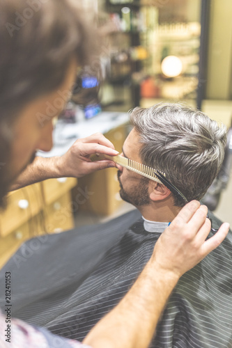 Barber cutting and modeling hair of his man client with scissors and comb.