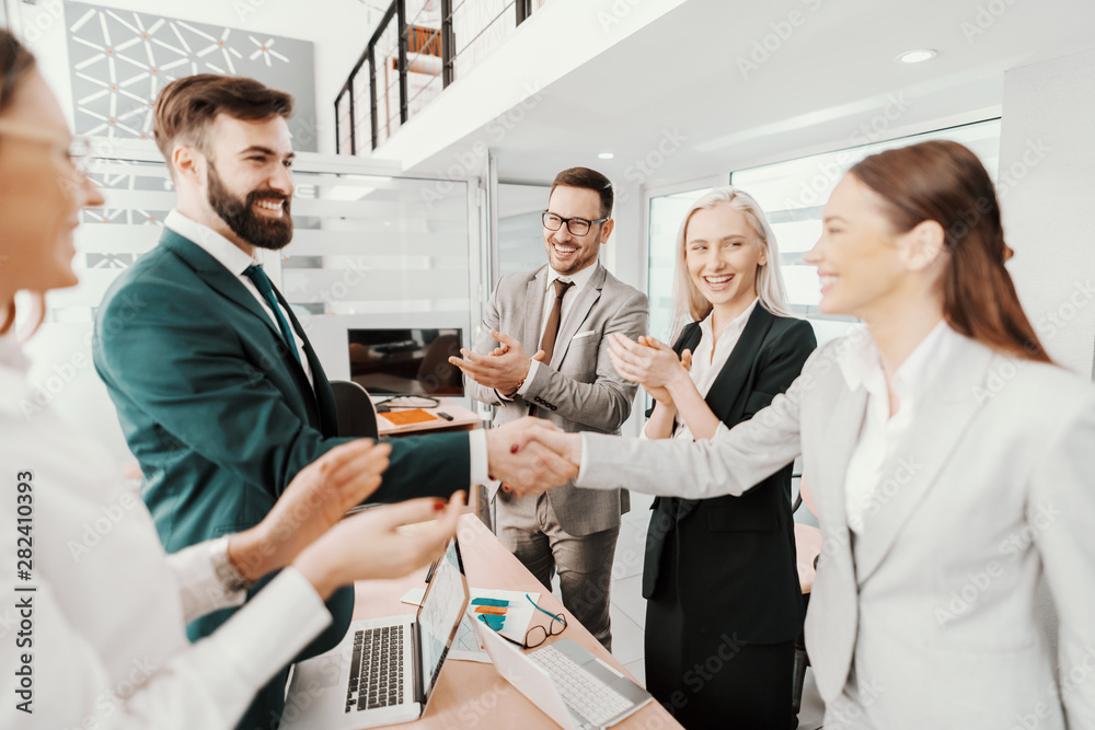 Obraz premium Two cheerful attractive Caucasian young business partners shaking hands in boardroom. Colleagues clapping.