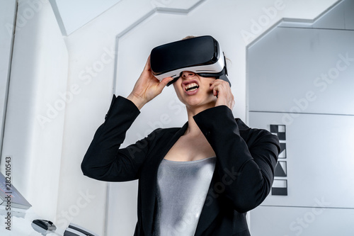 A girl in a black jacket standing in virtual reality glasses. Sees something disgusting, looking up and talking on a phone. Smartphone in her hand. Middle shot. Future concept