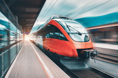 High speed orange train in motion on the railway station at sunset. Modern intercity passenger train with motion blur effect on the railway platform. Industrial. Railroad in Europe. Transport