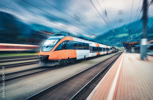 High speed orange train in motion on the railway station at sunset. Modern intercity passenger train with motion blur effect on the railway platform. Industrial. Railroad in Europe. Transport