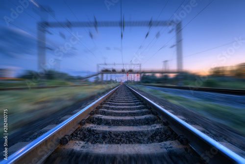 Railroad and blue sunset sky with clouds with motion blur effect. Industrial landscape with railway station and blurred background at twilight. Railway platform in move. Transportation. Speed motion