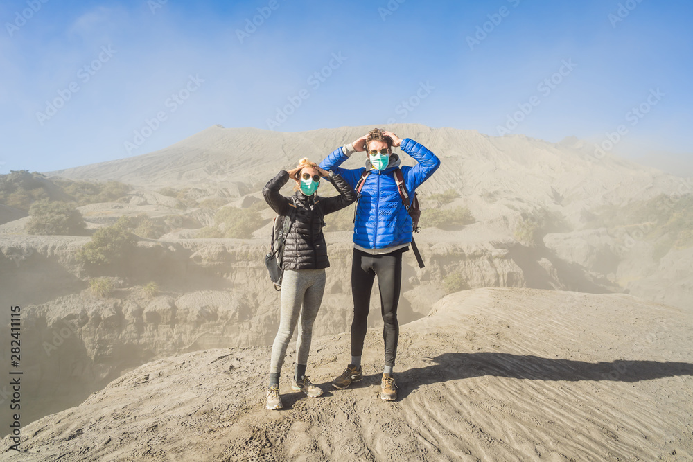 Young couple man and woman visit the Bromo volcano at the Tengger Semeru National Park on Java Island, Indonesia. They are scared of the eruption covering everything with dust and they wear safety