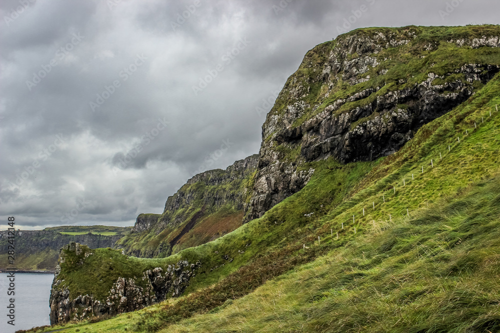 Cliffs near Giant's Causeway with dark grey clouds in the background and lively green grass in the foreground, Northern Ireland. Cliffs near Giant's Causeway with dark grey clouds in the background and lively green grass in the foreground, Northern Ireland.