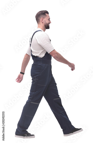 side view. smiling man in overalls confidently striding forward