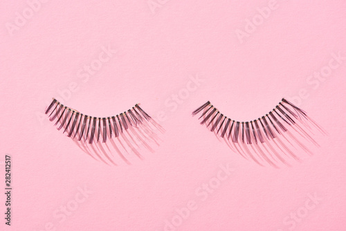 top view of false eyelashes on pink background with copy space