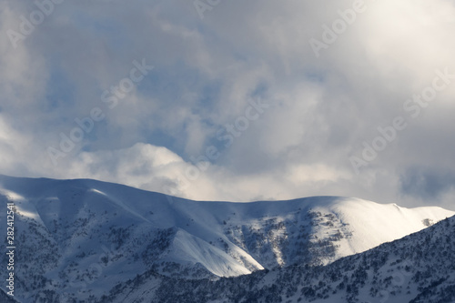 Snowy mountains with forest and sunlight cloudy sky