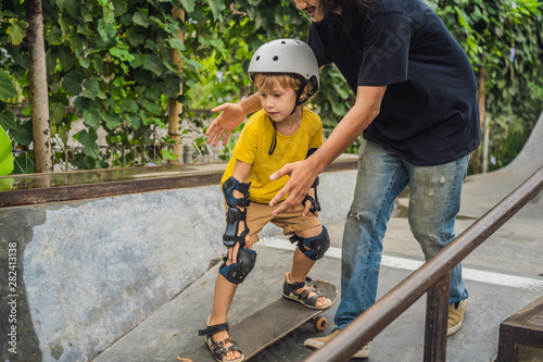 Athletic boy learns to skateboard with a trainer in a skate park. Children education, sports